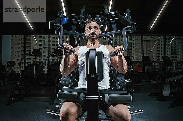 Hübscher junger Mann pumpt seine Schultern in einer speziellen Maschine. Fitness und Bodybuilding Konzept.