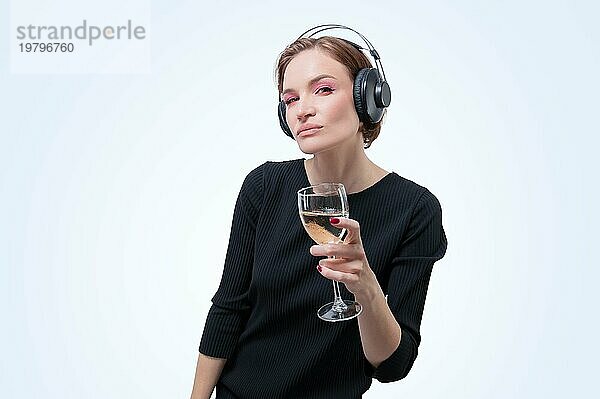 Porträt einer Frau mit professionellen Kopfhörern und einem Glas Wein in der Hand. Weißer Hintergrund. Dj Konzept. Gemischte Medien