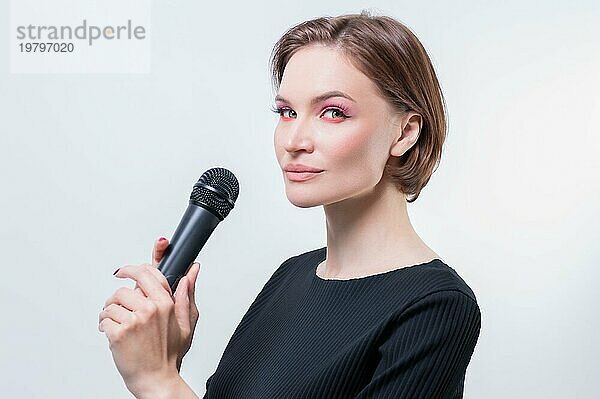 Porträt einer eleganten  stilvollen Frau mit einem Mikrofon. Weißer Hintergrund. Karaoke Konzept.