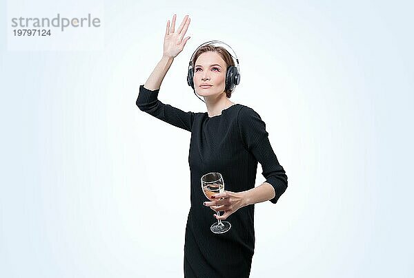 Porträt einer Frau mit professionellen Kopfhörern und einem Glas Wein in der Hand. Weißer Hintergrund. Dj Konzept. Gemischte Medien