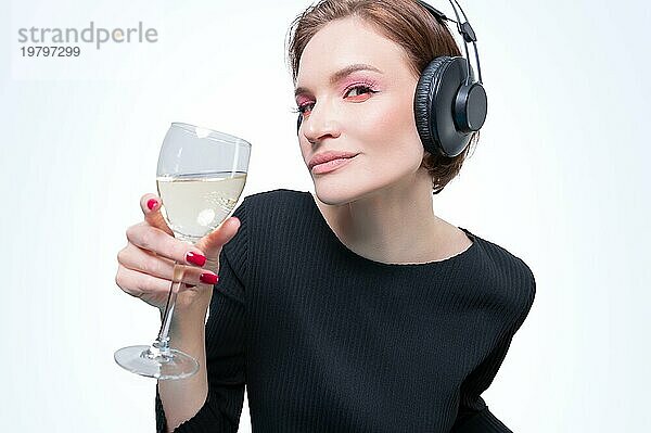 Porträt einer Frau mit professionellen Kopfhörern und einem Glas Wein in der Hand. Weißer Hintergrund. Dj Konzept. Gemischte Medien