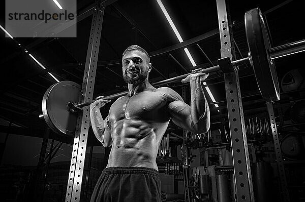 Muskulöser Mann posiert im Fitnessstudio mit einer Langhantel. Fitness Konzept.