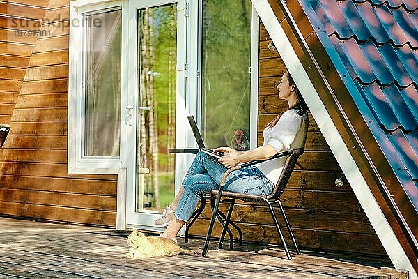 Digitaler Nomade mit Laptop auf der Veranda eines kleinen Blockhauses