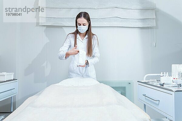 Der Arzt bereitet sich auf den Empfang einer Patientin in einem Schönheitssalon vor. Die Frau deckt die Liege mit einer schützenden  hygienischen weißen Decke zu. Gemischte Medien