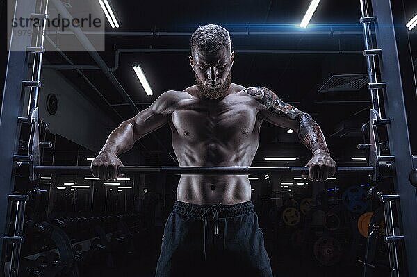 Porträt eines Sportlers  der vor einer Langhantel im Fitnessstudio steht. Bodybuilding und Fitness Konzept.