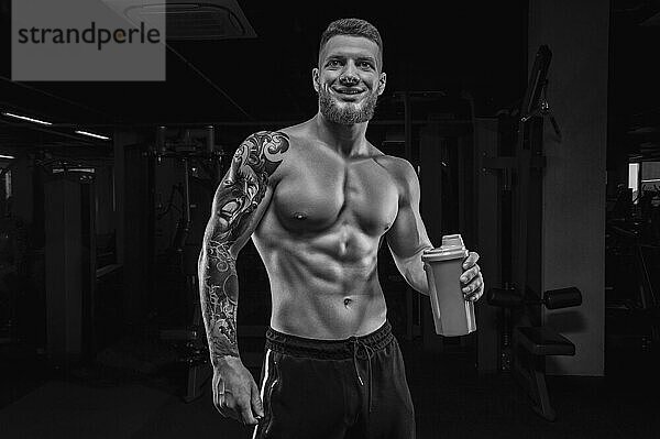 Porträt eines Sportlers  der mit einem Shaker im Fitnessstudio steht. Bodybuilding und Fitness Konzept.