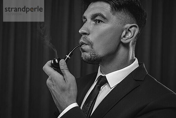 Bild eines eleganten Mannes in einem Anzug  der eine Pfeife raucht. Konzept für geschäftlichen Erfolg.
