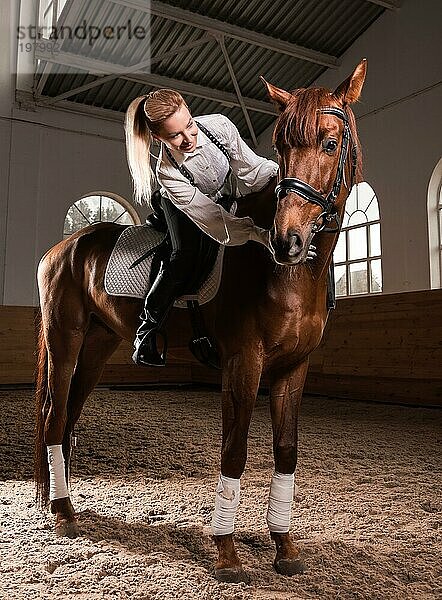 Bild einer Frau  die ein Vollblutpferd reitet. Der Hintergrund ist eine Rennarena.