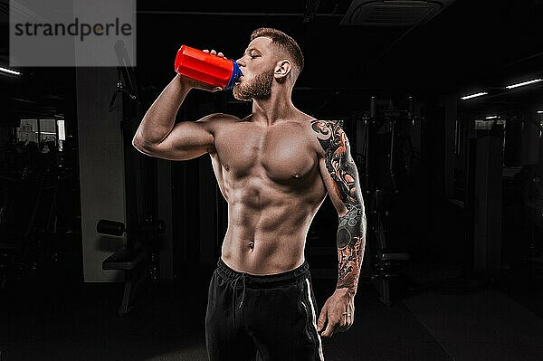 Porträt eines Sportlers  der aus einem Shaker im Fitnessstudio trinkt. Bodybuilding und Fitness Konzept.