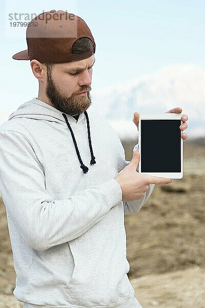 Nahaufnahme Porträt eines Hipsters mit einer braunen Mütze im Freien  der ein weißes Tablet PC in den Händen hält. Ein bärtiger Mann schaut auf das Tablet. Hintergrund unscharf
