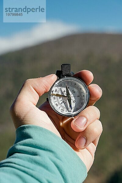 Nahaufnahme Die Hand eines Mannes hält einen Taschenkompass vor dem Hintergrund von Bergen und Wäldern. Das Konzept der Outdoor Navigation