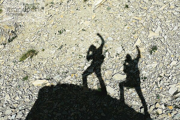 Zwei Schatten von Fotografen auf der Erde  die mit erhobenen Händen bergauf gehen und über Sieg und Erfolg schreien. Silhouetten von zwei Menschen  die bergauf gehen