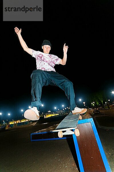 Ein junger Skater vollführt den Trick des nächtlichen Gleitens in einem Skatepark inmitten der brennenden Lichter der Lichtmasten