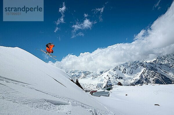 Athleten Skifahrer Freestyle Springen in orange Skianzug in verschneiten Bergen an einem sonnigen Tag