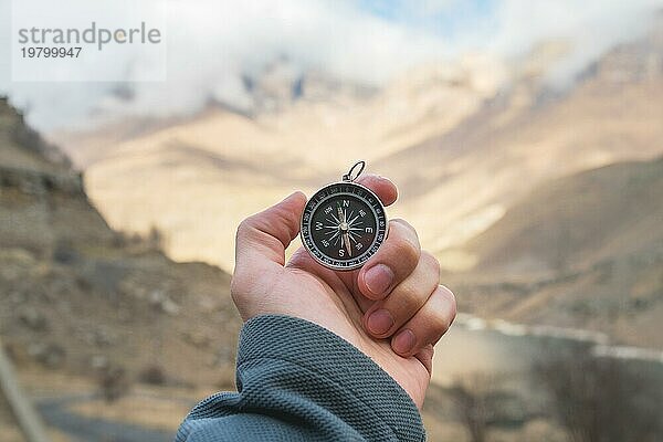 Ein männlicher Wanderer sucht mit einem Magnetkompass in den Bergen im Herbst nach einer Richtung. Aufnahme aus der Vogelperspektive. Männerhand mit Uhrenarmband hält einen Kompass