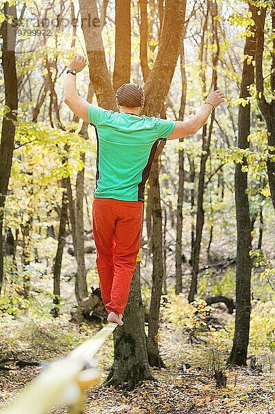 Ein bärtiger Mann mittleren Alters geht an einem sonnigen Nachmittag im Herbstwald an einer Slackline entlang. Das Konzept der Freizeit und Erholung von aktiven Menschen mittleren Alters