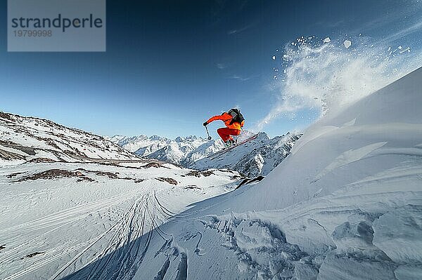 Ein männlicher Skisportler springt an einem sonnigen Tag von einem schneebedeckten Hang vor dem Hintergrund einer Berglandschaft mit schneebedeckten Bergen. Das Konzept des Wintersports