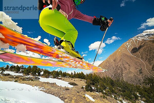 Mädchen Skifahrer im Flug nach dem Sprung von einem Kicker im Frühjahr vor dem Hintergrund der Berge und blaün Himmel. Nahaufnahme mit Weitwinkel. Das Konzept der Schließung der Skisaison und Skifahren im Frühjahr