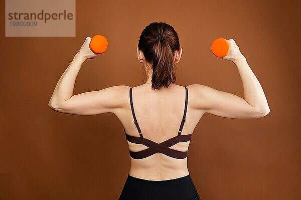 Porträt einer Frau Fitness Sportler mit einem Hintern. Kaukasische Frau Fitness Sportler zeigt eine Geste der Stärke. Studio Foto. Auf einem braunen Hintergrund