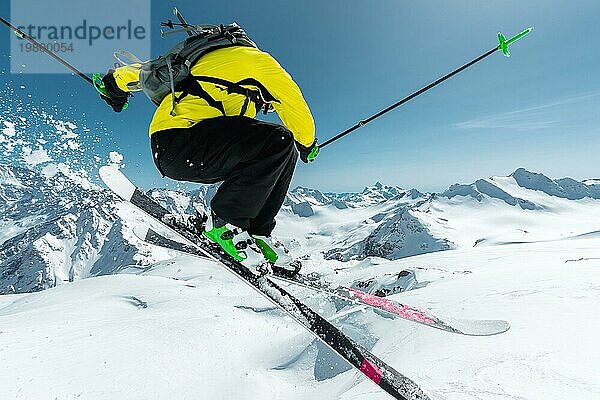 Ein Skifahrer in voller Sportausrüstung springt von der Spitze des Gletschers in den Abgrund  vor dem Hintergrund des blaün Himmels und der schneebedeckten Berge des Kaukasus. Blick von hinten. Elbrus Gebiet. Russland