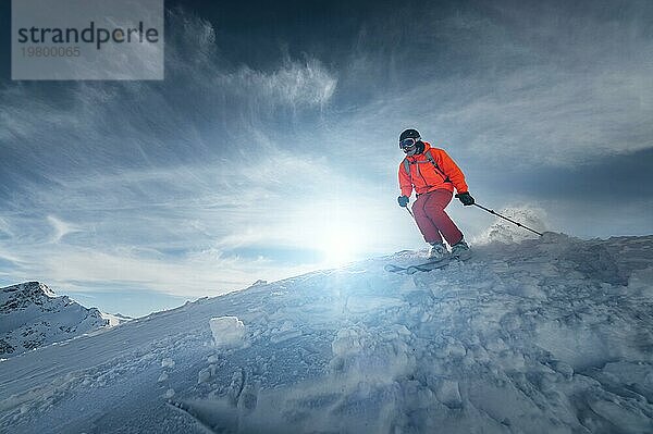 Ein Skifahrer fährt an einem sonnigen Tag bei Sonnenuntergang auf einer verschneiten Piste vor der Kulisse der Berge. Das Konzept des Skifahrens im Winter