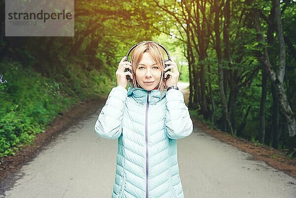 Porträt einer schönen jungen Frau mit Kopfhörern  die draußen im Wald Musik hört. Fröhliche Musik