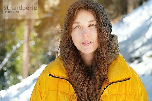 Schöne freundliche kaukasische junge Frau in Winterkleidung lächelnd niedlich Blick in die Kamera in einem Winterwald durch Schnee umgeben