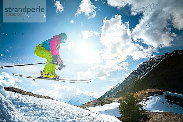 Mädchen Skifahrer im Flug nach dem Sprung von einem Kicker im Frühjahr vor dem Hintergrund der Berge und blaün Himmel. Nahaufnahme mit Weitwinkel. Das Konzept der Schließung der Skisaison und Skifahren im Frühjahr