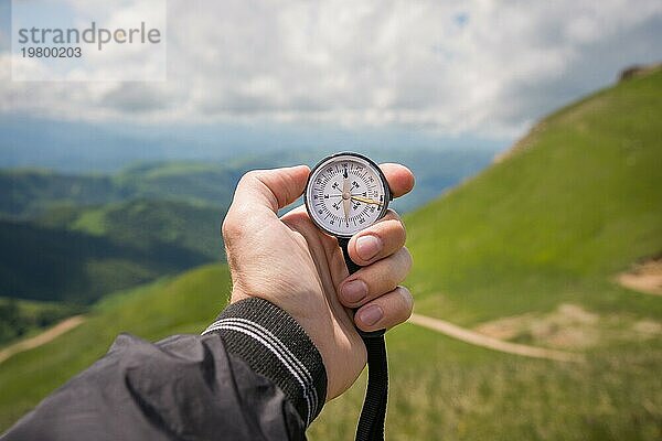 Ein Mann die Hand eines Touristen mit einem authentischen Kompass auf dem Hintergrund einer Bergstraße Landschaft