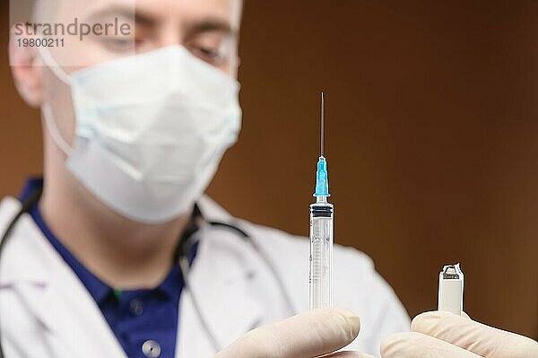 Junger kaukasischer Arzt im weißen Kittel  der eine Spritze mit einem Impfstoff hält. Fokus auf die Spritze