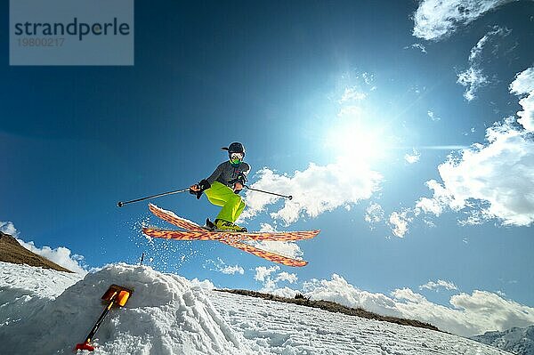 Mädchen Skifahrer im Flug nach dem Sprung von einem Kicker im Frühjahr vor dem Hintergrund der Berge und blaün Himmel. Nahaufnahme mit Weitwinkel. Das Konzept der Schließung der Skisaison und Skifahren im Frühjahr