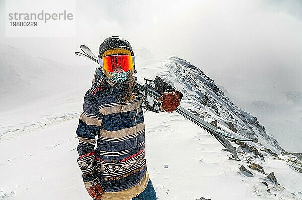 Porträt einer hübschen und aktiven Skifahrerin  die eine Maske trägt und Skier in den Händen hält  aktiver Winterurlaub. Extrem Lifestyle Konzept