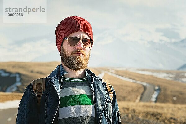 Modeporträt eines bärtigen jungen Mannes mit Sonnenbrille  Rucksack und Hut auf einem Hintergrund mit Copyspase in den Bergen bei Sonnenuntergang  Ein selbstbewusster Mann mit einem Bart