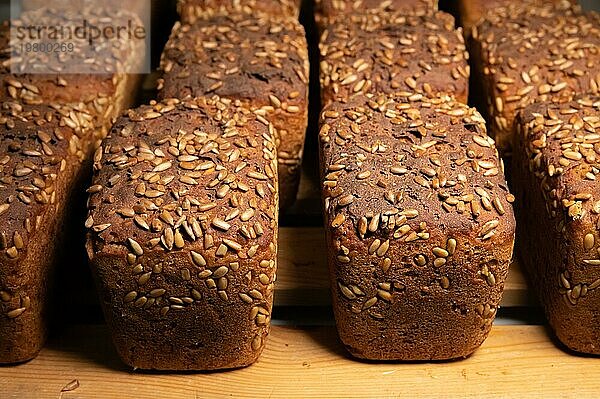 Nahaufnahme von frischen  braunen Roggenbrotlaiben in Form von Ziegelsteinen mit Sonnenblumenkernen auf der Kruste. Liegen auf einem Holzgestell