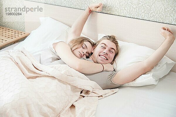 Ein junges Paar von langhaarigen attraktiven Männern und Frauen im Bett. Ein junger Mann liegt ausgestreckt im Bett neben seiner jungen Frau. Hochzeitsmorgen