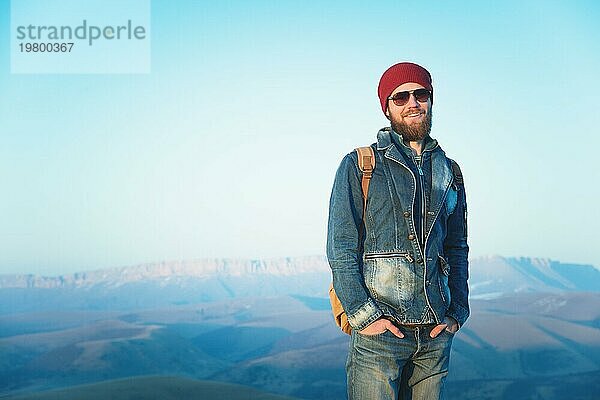 Hipster junger Mann mit Bart und Schnurrbart und Sonnenbrille posiert vor dem Hintergrund der Berge