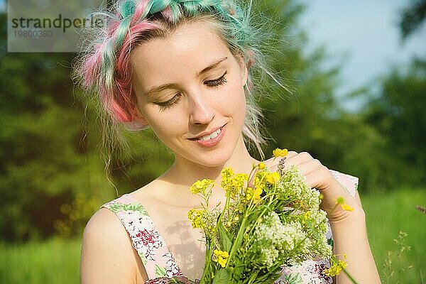 Porträt eines jungen  glücklich lächelnden Mädchens in einem Baumwollkleid mit einem Strauß Wildblumen