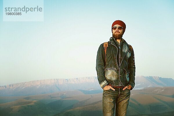 Hipster junger Mann mit Bart und Schnurrbart und Sonnenbrille posiert vor dem Hintergrund der Berge