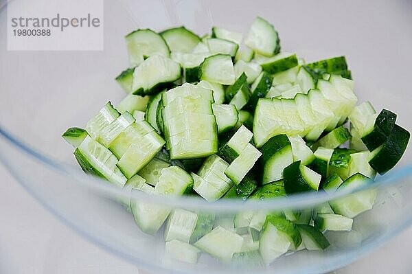Frische Gurke in Scheiben geschnitten für die Zubereitung von Gemüsesalat in einer transparenten Glasschale auf dem Küchentisch. Geringe Tiefenschärfe