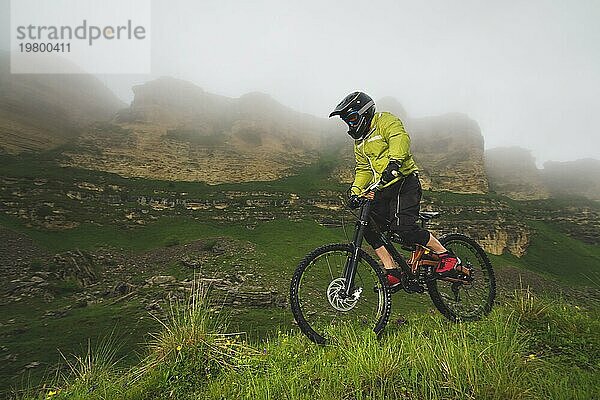 Ein Mann mit Berghelm und Mountainbike fährt bei bewölktem Wetter durch die schöne Natur bergab