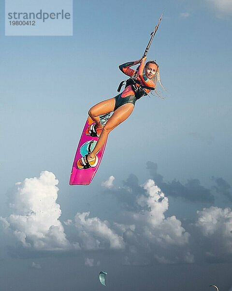 Professionelle Athleten Kitesurfer junge kaukasische Frau einen Trick in der Luft vor dem Hintergrund des Sonnenuntergangs Himmel und Wolken zu tun. Professionelle Kitesurfen und Kite Kultur Ausbildung