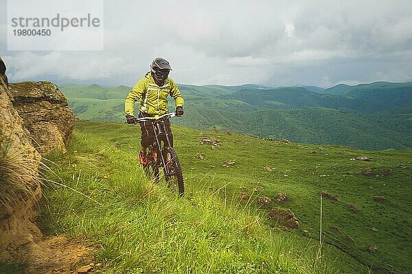 Ein Mann mit Berghelm und Mountainbike fährt bei bewölktem Wetter durch die schöne Natur bergab