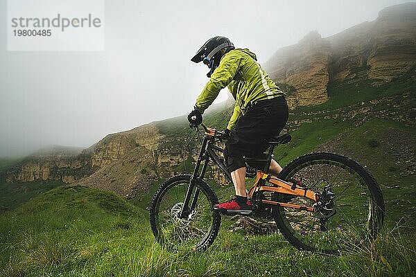 Ein Mann mit Berghelm und Mountainbike fährt bei bewölktem Wetter durch die schöne Natur bergab