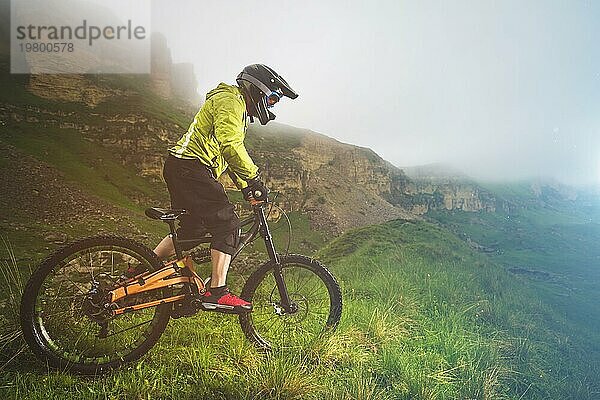 Ein Mann mit Berghelm und Mountainbike fährt bei bewölktem Wetter durch die schöne Natur bergab