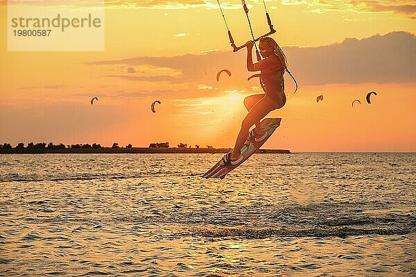 Junge Frau professionelle Kiter führt einen schwierigen Trick in der Luft auf einem schönen Hintergrund des Sonnenuntergangs und Meer