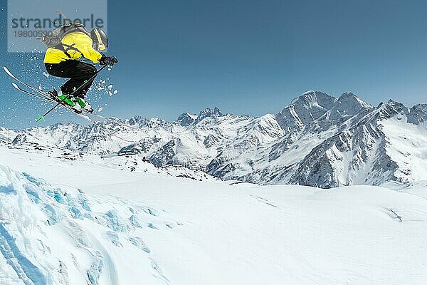 Ein Skifahrer in voller Sportausrüstung springt von der Spitze des Gletschers in den Abgrund vor dem Hintergrund des blaün Himmels und der schneebedeckten Berge des Kaukasus. Elbrus Gebiet. Russland