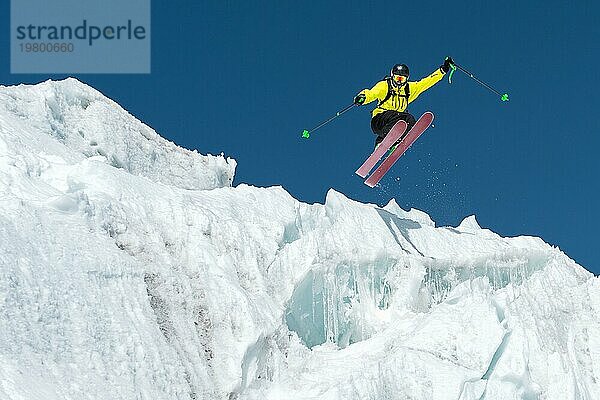 Ein springender Skifahrer springt von einem Gletscher vor einem blaün Himmel hoch in den Bergen. Professionelles Skifahren