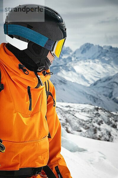 Nahaufnahme Ein professioneller Skifahrer in roter Jacke  Helm und Maske steht auf einer Piste vor der Kulisse eines Gletschers und epischer Berge und zeigt mit einem Skistock auf eine Bergkette Freeride Konzept