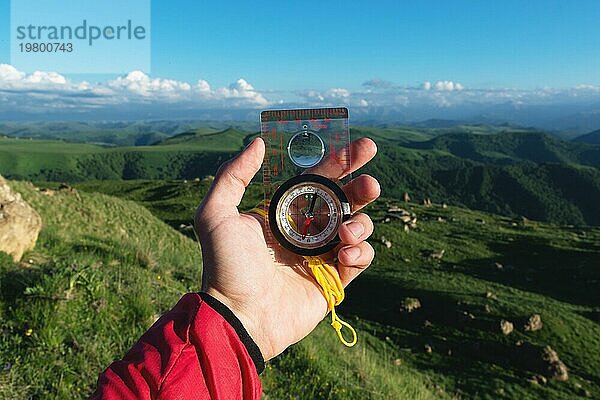 Mann auf der Suche nach der Richtung mit einem Kompass in der Hand in den sommerlichen Bergen Ansicht. Richtungssuche