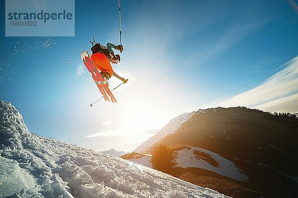 Mann Skifahrer im Flug nach dem Sprung von einem Kicker im Frühjahr vor dem Hintergrund der Berge und blaün Himmel. Nahaufnahme mit Weitwinkel. Das Konzept der Schließung der Skisaison und Skifahren im Frühjahr